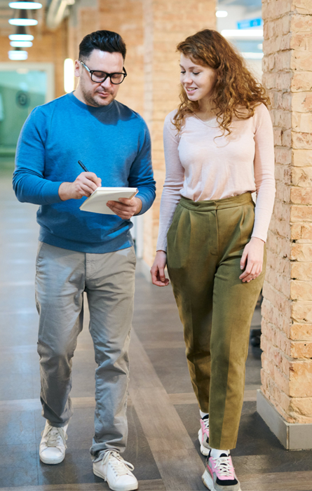 A professional man and woman walking together in a modern office lobby, symbolizing business travel and collaboration.
